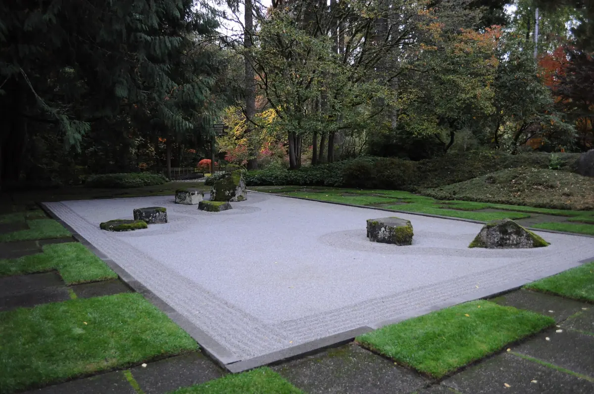 Raked gravel garden with rocks and lawn edges under tall trees
