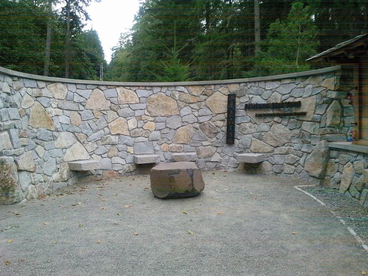 Curved stone wall with benches at the memorial in a forest setting
