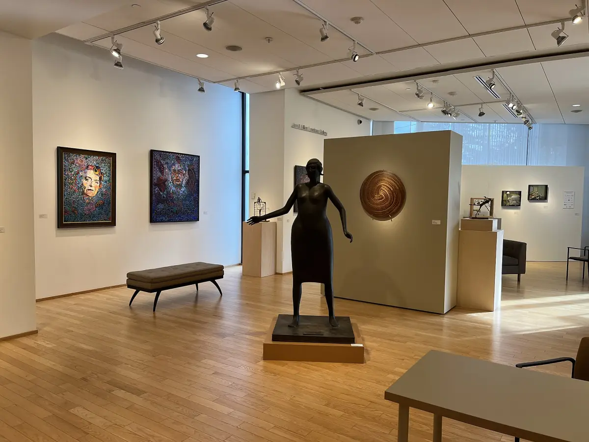 Bright gallery room with a bronze figure and framed paintings on white walls