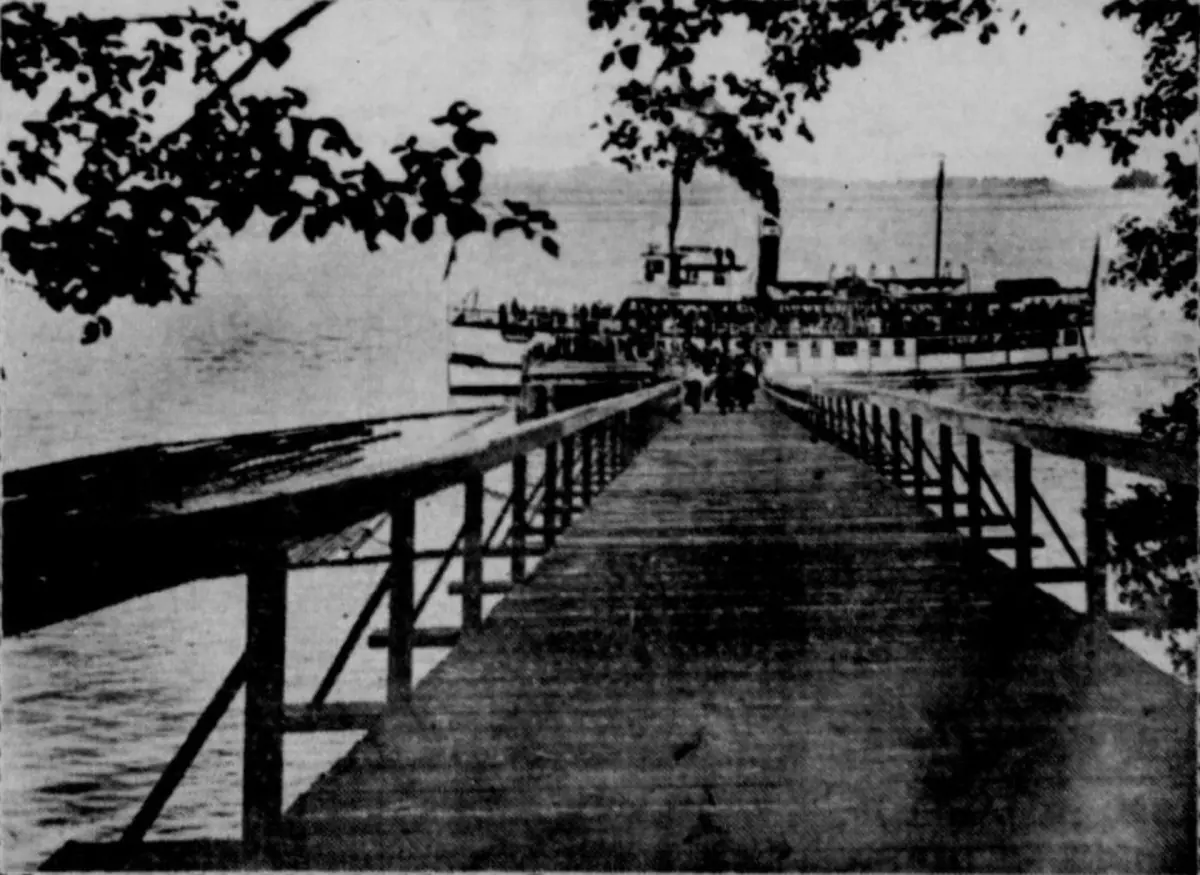 Historic black and white photo of a steamboat at a wooden dock